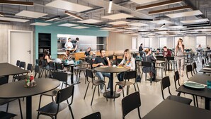 A spacious cafeteria with multiple tables and chairs, a kitchen area in the background, and a modern ceiling design.