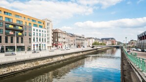 A canal with buildings on either side, including a modern building with a sign that reads "DeHoos."