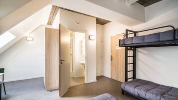 Een studentenkamer met stapelbedden, een bureau en een dakraam.