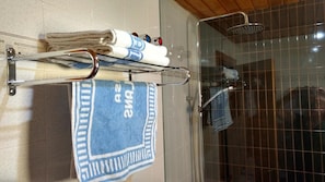 A bathroom with a glass shower enclosure, a towel rack with folded towels, and a blue towel with "A2" text. - Apartamentos Casa Morlans (Panticosa)