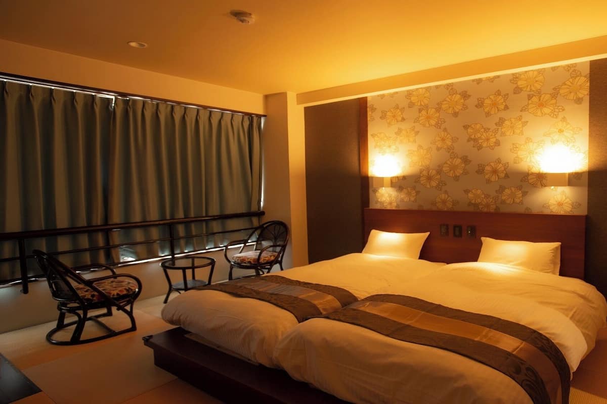 A hotel room with a large bed, two bedside lamps, a chair, and a window with curtains.
