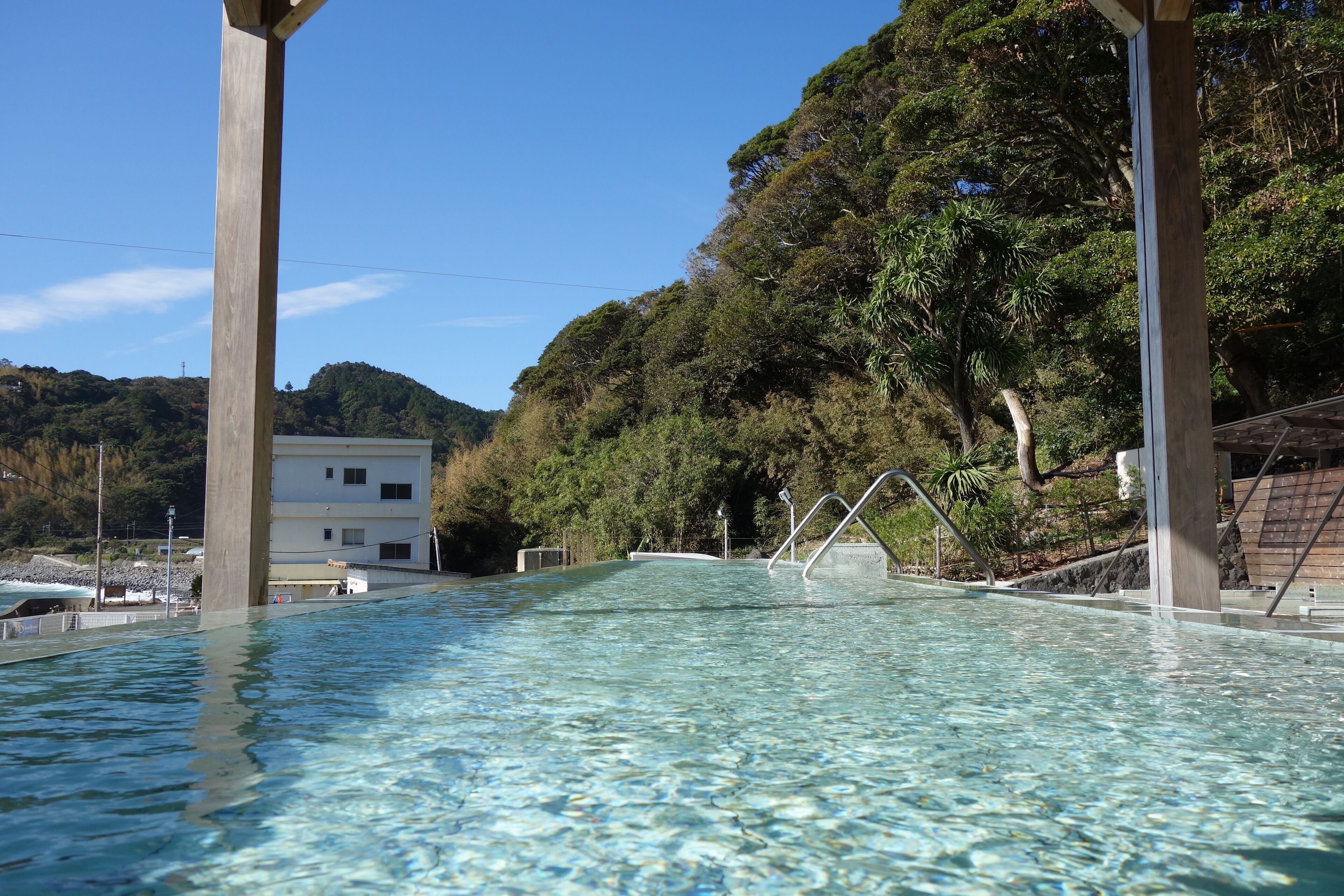 Piscina cristalina con estructuras de madera, rodeada de exuberante vegetación y una ladera.