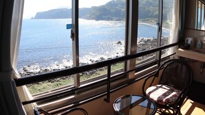 A room with a large window overlooking a beach and cliffs. There is a chair and a small table near the window. - RYUGU no TSUKAI (Higashiizu)