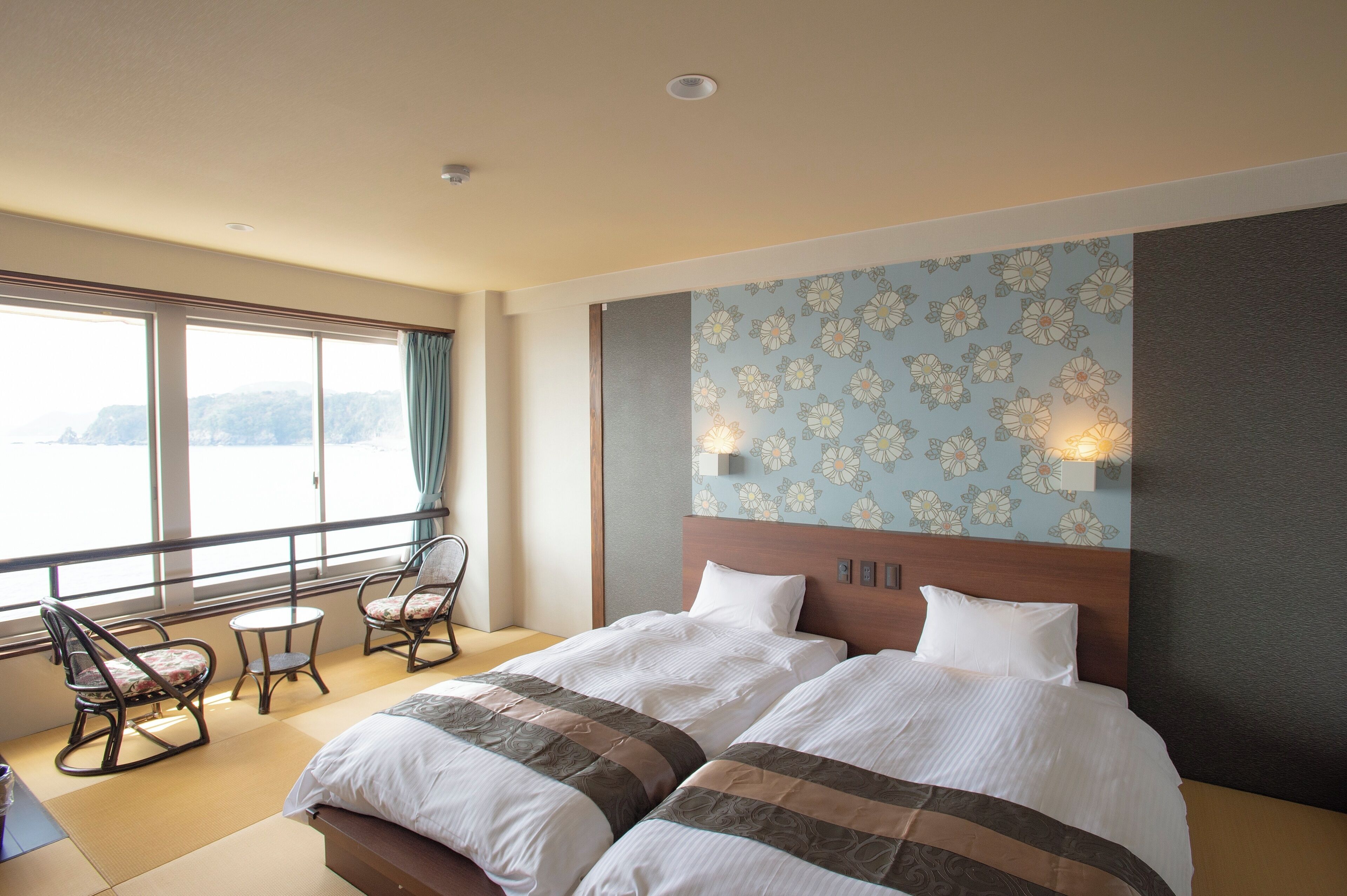 A hotel room with a large bed, two chairs, a small table, and a view of the sea.