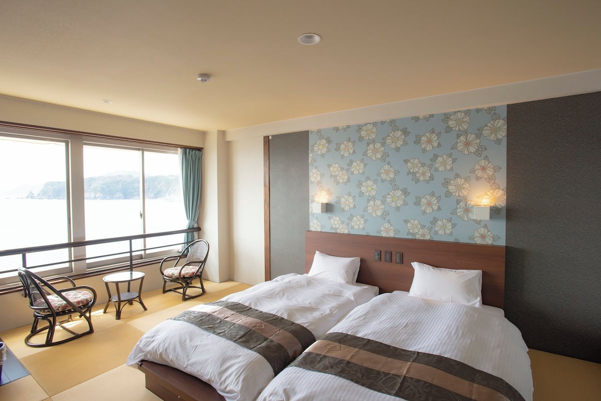 A hotel room with a large bed, two chairs, a small table, and a view of the sea.