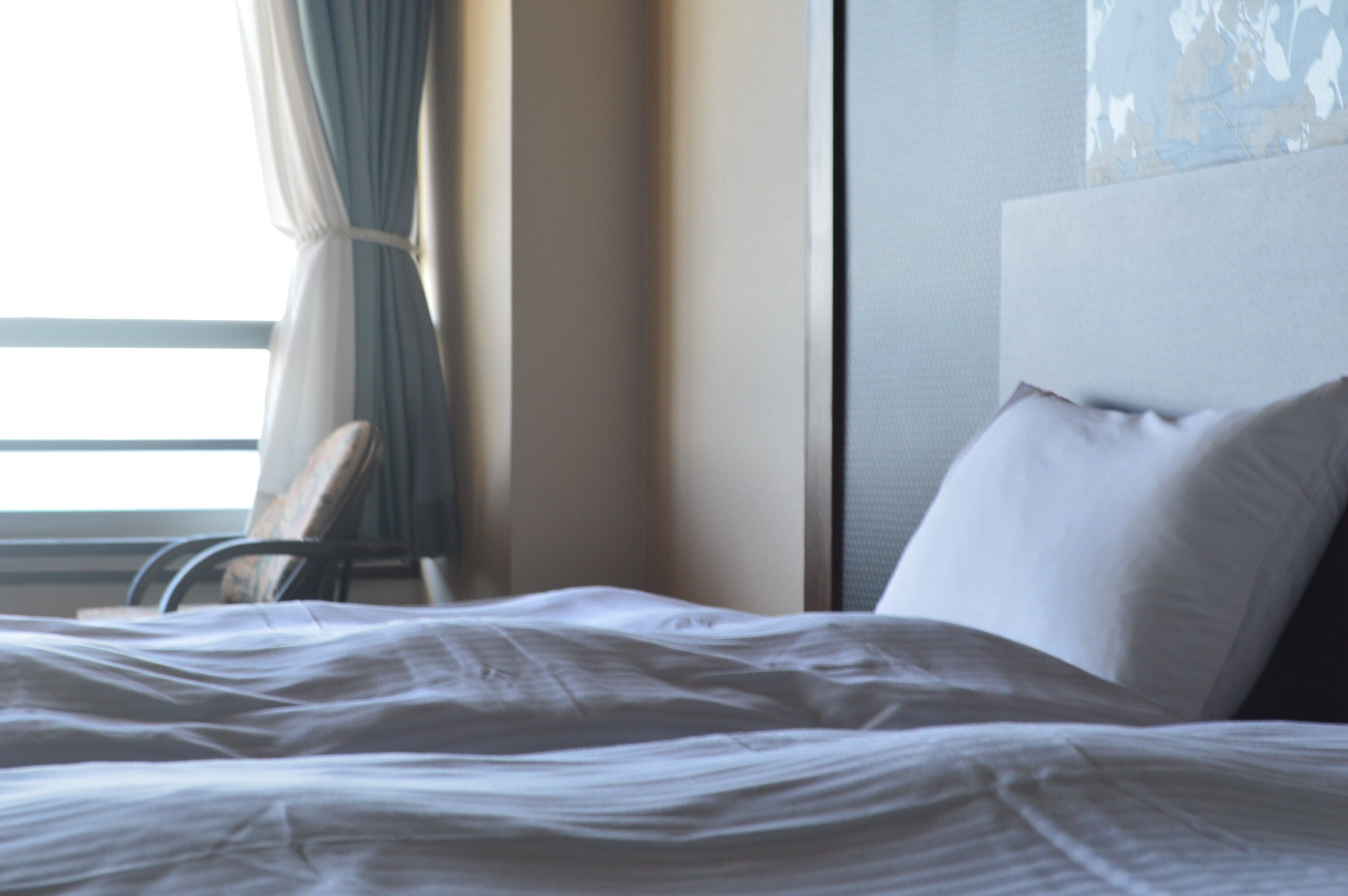A hotel room with a bed, a chair, and a window with curtains.