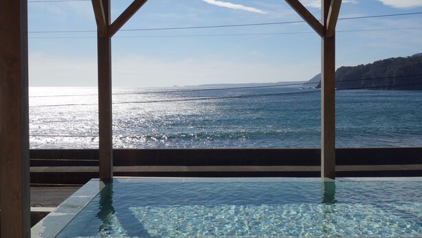 A view from a wooden structure with a pool, overlooking a body of water and a distant coastline. - RYUGU no TSUKAI (Higashiizu)
