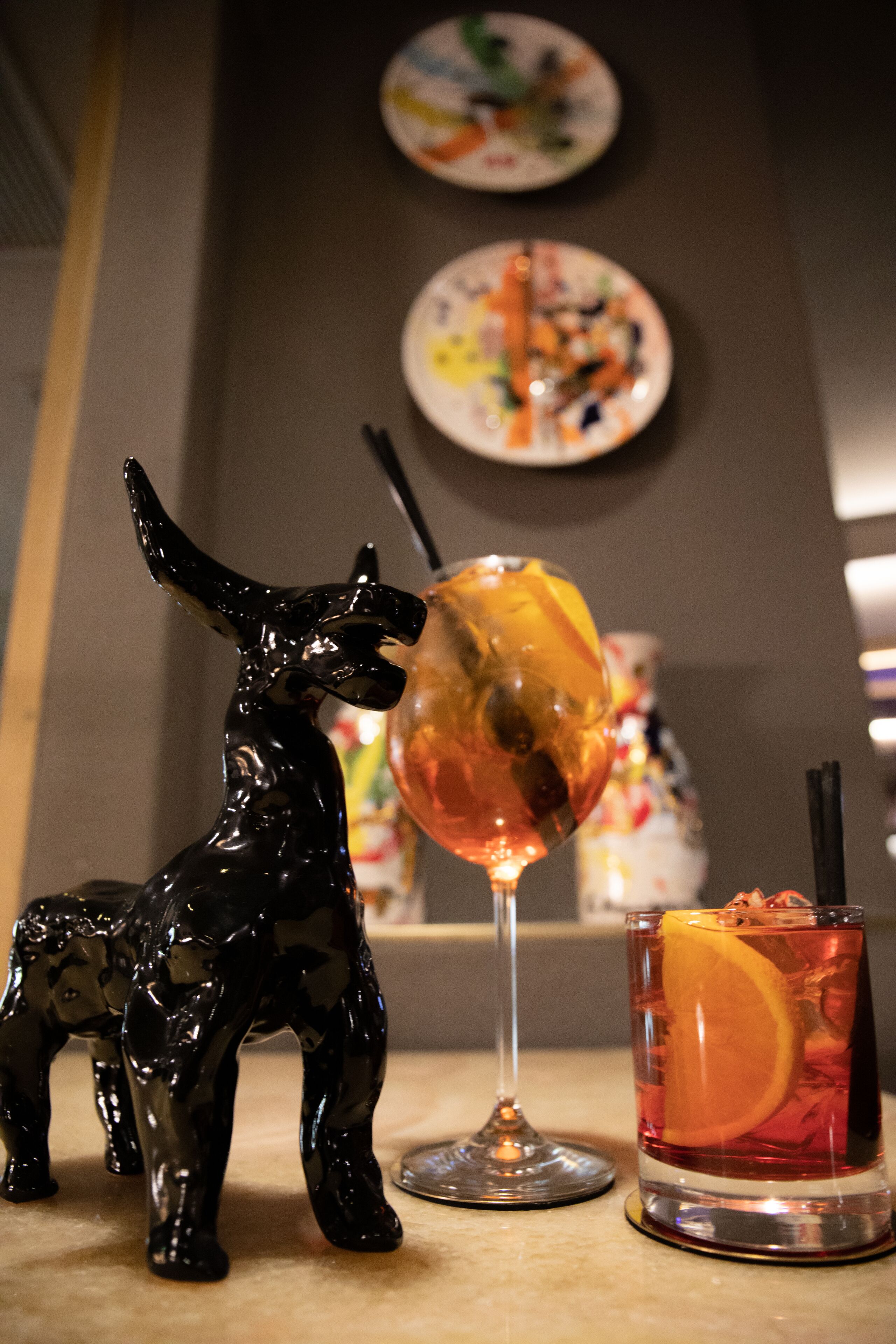 Una figura de un caballo negro, un vaso con una rodaja de naranja y una copa de vino sobre una mesa.