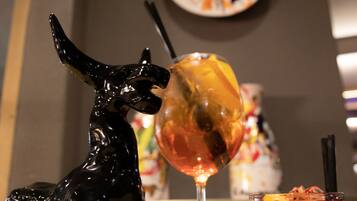 Una figura de un caballo negro, un vaso con una rodaja de naranja y una copa de vino sobre una mesa.