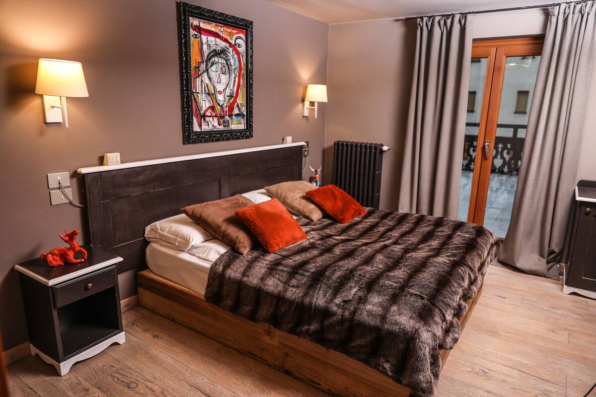 Une chambre à coucher avec un lit en bois, deux lampes de chevet, un radiateur et une fenêtre avec des rideaux.