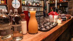 Eine Bar mit verschiedenen Flaschen und Gläsern, einer Uhr an der Wand und einem Tablett mit leeren Gläsern.