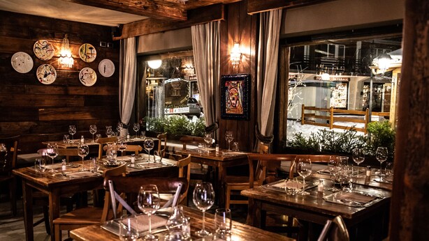 Ein Restaurant mit Holztischen und -stühlen, Weingläsern und einer Kristallleuchter.