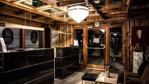Ein Hotel-Empfangsbereich mit Holzvertäfelung, einer Kristallleuchtre, einer Rezeption und einer Sitzecke mit Tisch und Stühlen.