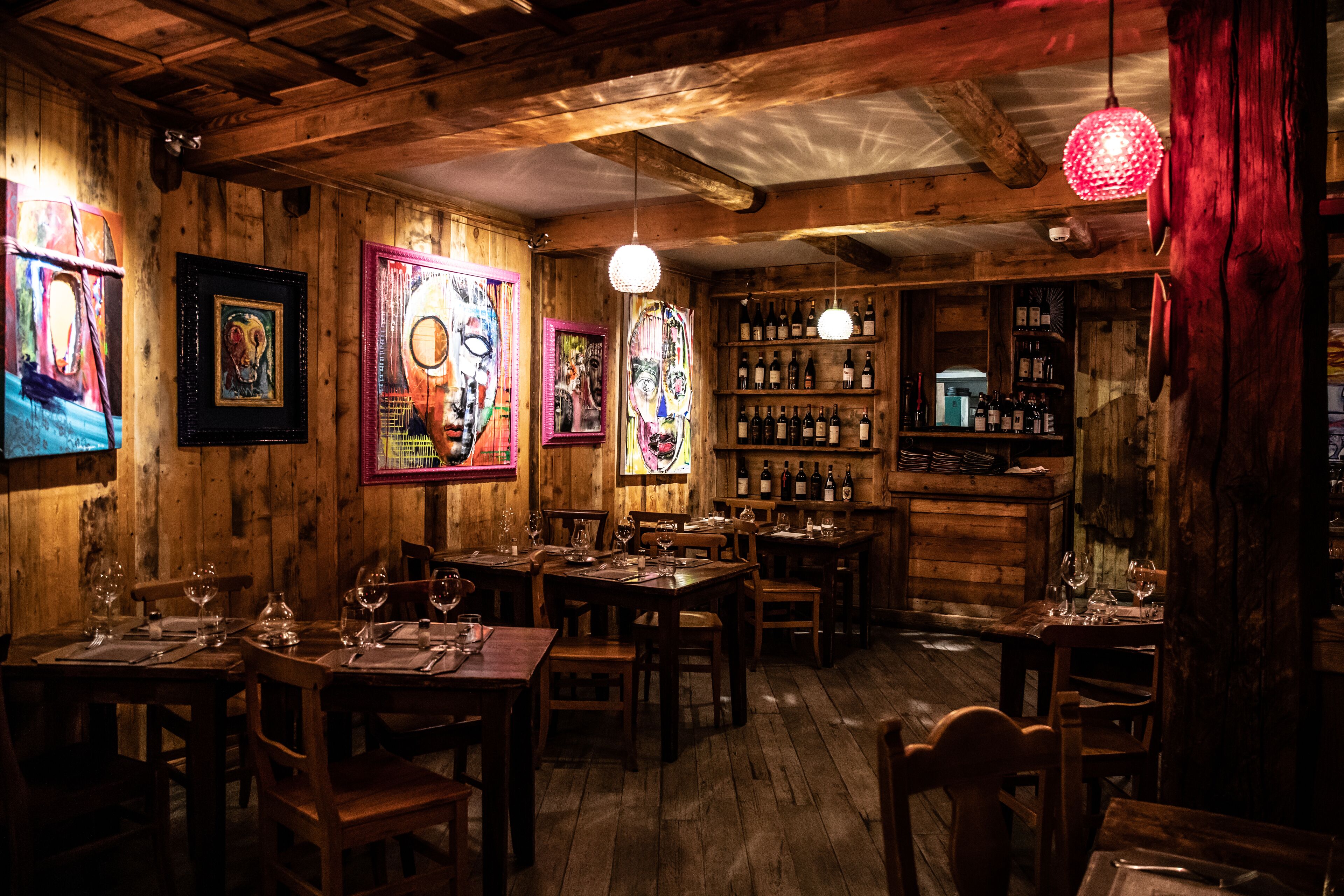 Een rustiek houten interieur met meerdere eettafels gedekt voor gasten, houten wanden en een bar met flessen.