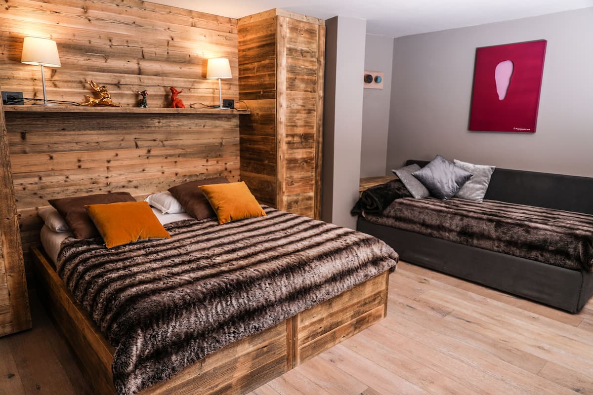 Une pièce avec un mur en bois, un lit recouvert d’une couverture à rayures, un canapé et deux lampes fixées au mur.