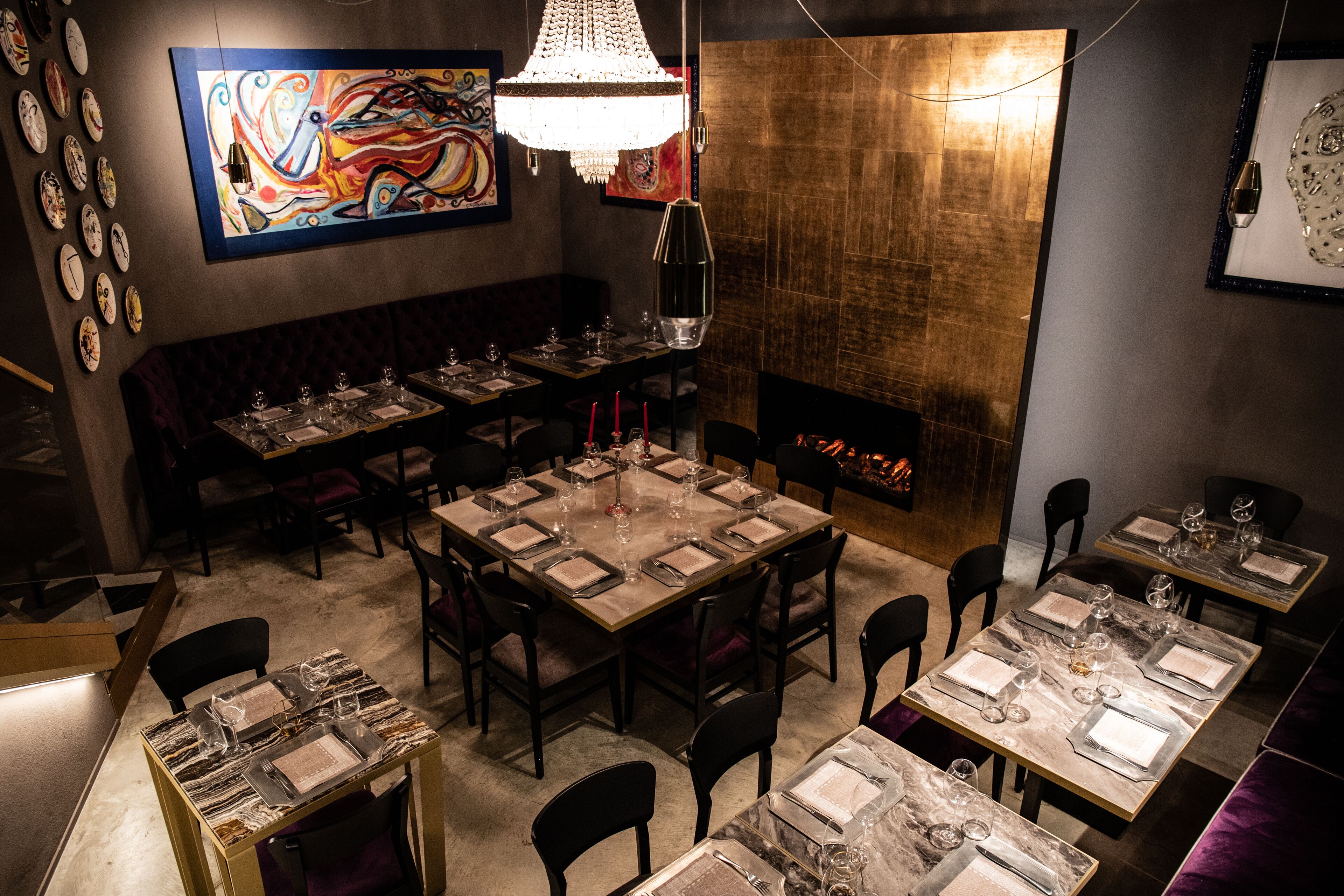 A restaurant with multiple tables set for dining, a large chandelier, and a fireplace.