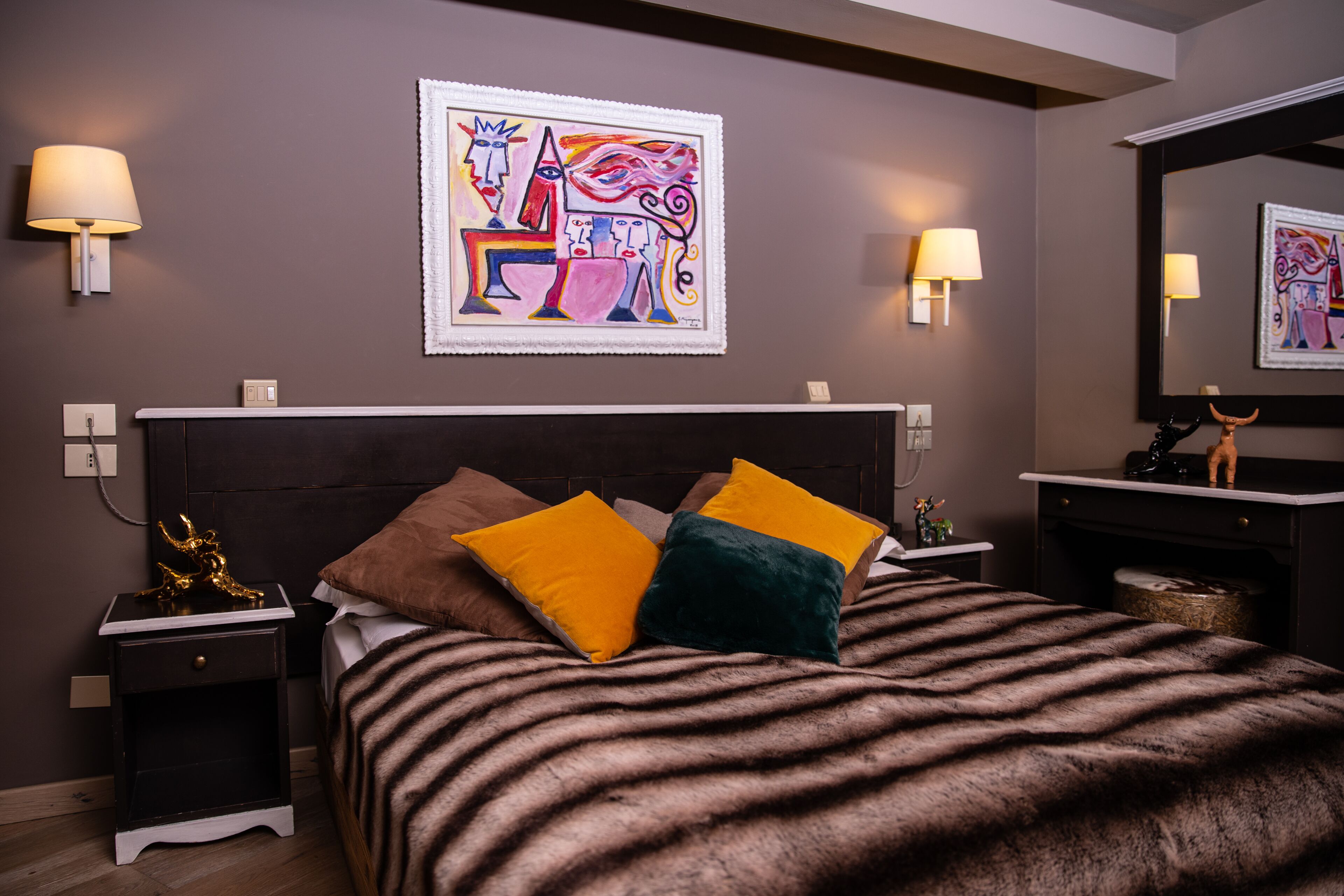 A modern bedroom with a large bed, two nightstands, a mirror, and abstract artwork on the wall.