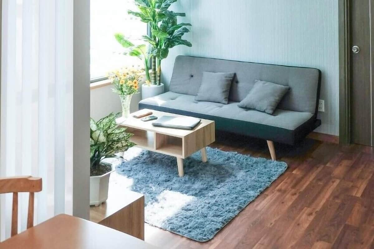 A modern living room with a grey sofa, a coffee table, and a blue rug. There are three wall-mounted paintings of deer, a hanging light fixture, and a large window with curtains.
