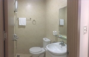 A small bathroom with a toilet, a sink, a shower, and a mirror. - Beach City Apartment (Bac Nha Trang)