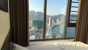 A hotel room with a large window offering a view of a cityscape and mountains. - Beach City Apartment (Bac Nha Trang)