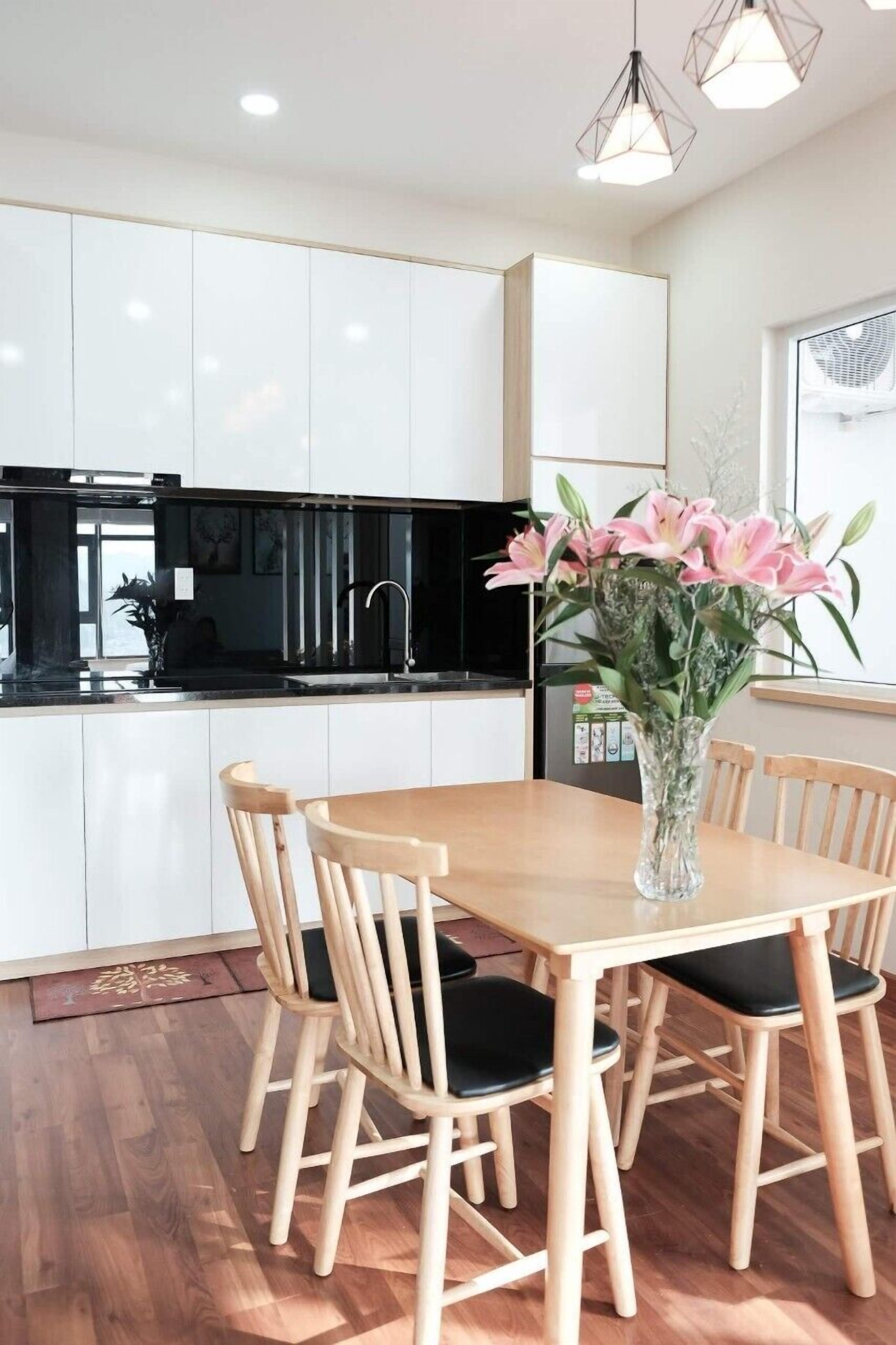 Una cocina moderna con armarios blancos, una mesa de comedor de madera con sillas y un jarrón de flores rosas.
