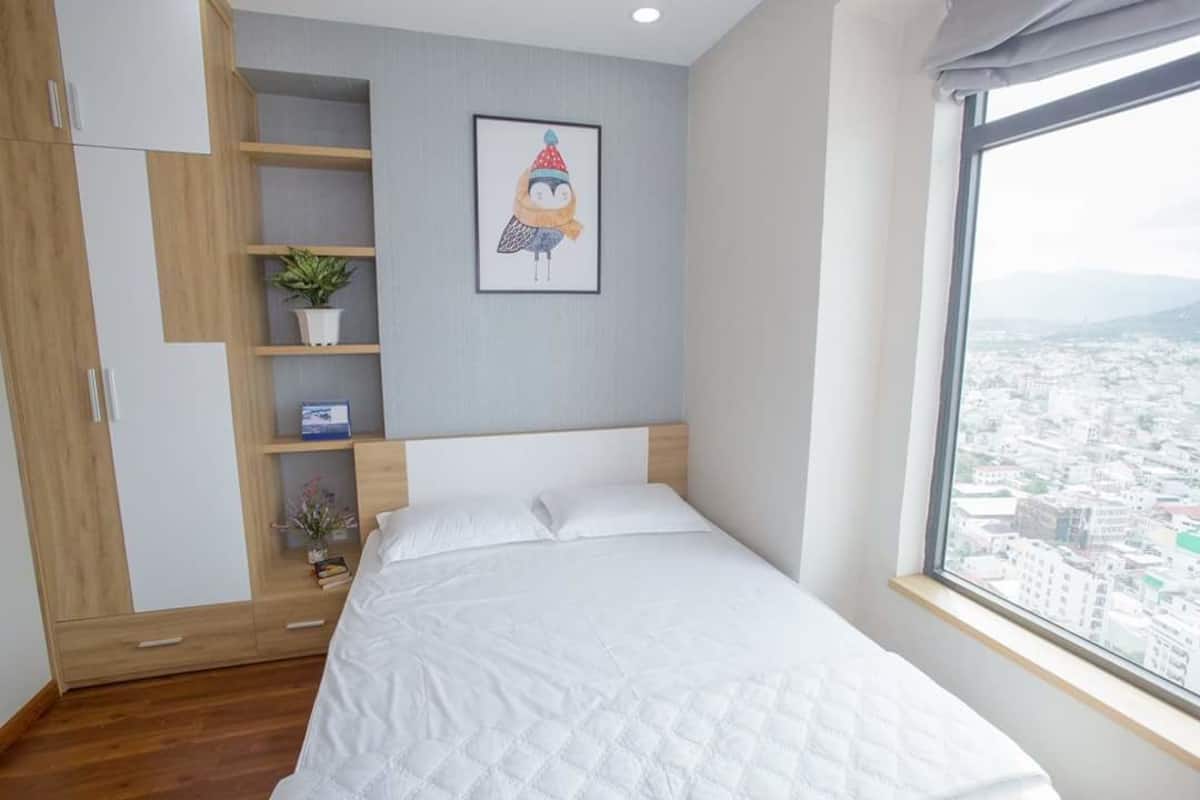A bedroom with a bed, a wardrobe, a shelf with a plant, and a framed picture on the wall.