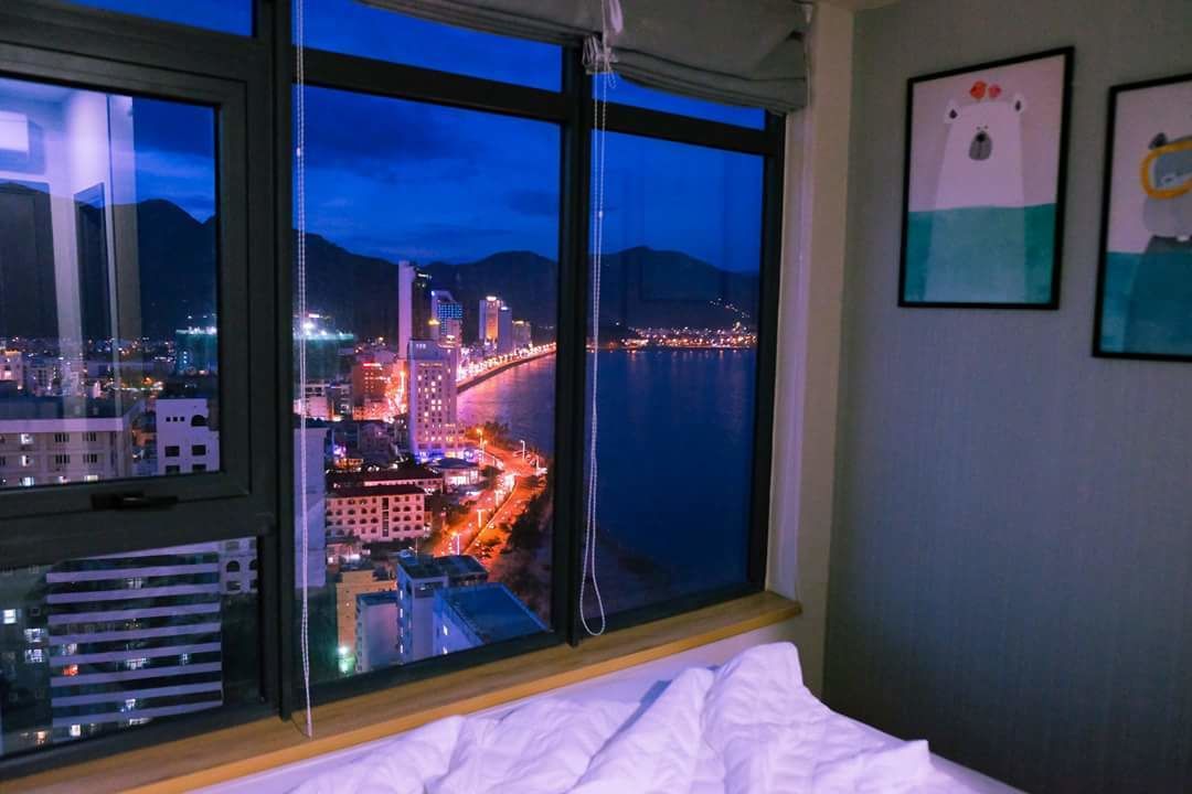 Quarto de hotel com uma janela grande com vista para a paisagem urbana à noite.