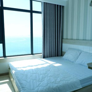 A hotel room with a large window, a bed with white bedding, and a striped curtain. - Beach City Apartment (Bac Nha Trang)