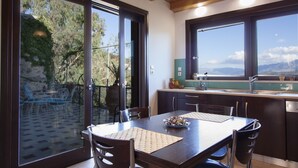 A modern kitchen with large windows, a dining area with a table and chairs, and a view of the outdoors. - Malaxiana Houses (Chania)