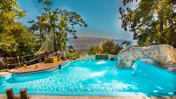 A swimming pool with a view of mountains, surrounded by trees and a rocky structure. - Malaxiana Houses (Chania)