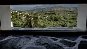 A view from a window with a stone floor, overlooking a green landscape with trees and distant mountains. - Malaxiana Houses (Chania)