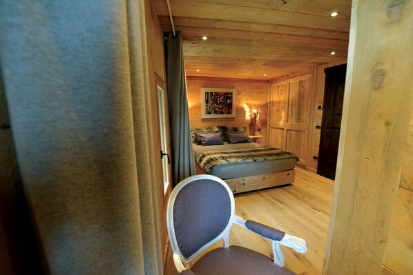 A cozy wooden cabin bedroom with a bed, a chair, and a painting on the wall.