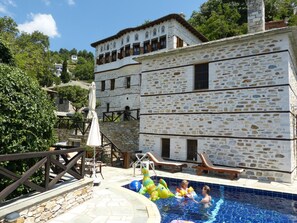 A stone building with a pool area, including lounge chairs and a children's inflatable pool. - Ta Xelidonakia (South Pelion)