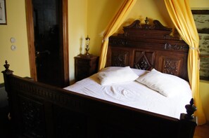A wooden four-poster bed with white linens, a nightstand with a lamp, and yellow curtains. - Ta Xelidonakia (South Pelion)