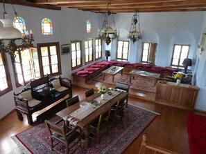 A spacious living room with a wooden dining table, cushioned seating, and a large window with multiple panes. - Ta Xelidonakia (South Pelion)