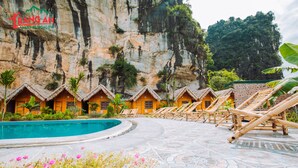 A resort with thatched-roof cabins, a pool, and a mountainous backdrop. - Trang An Valley Bungalow (Tay Hoa Lu)