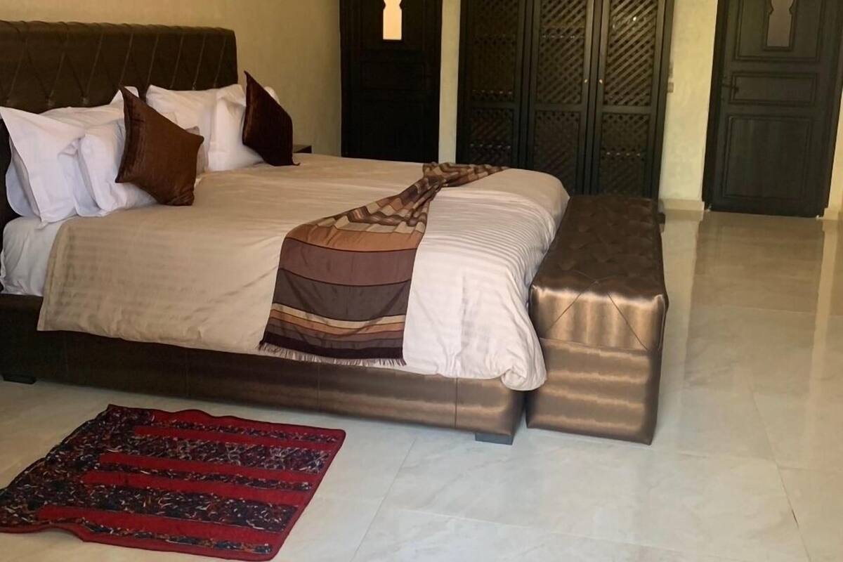 A bedroom with a large bed, a bedside table, a nightstand, a carpet, and a chandelier.