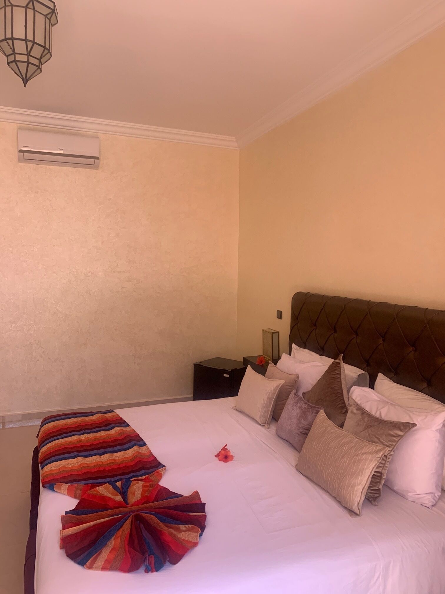 Quarto de hotel com uma cama grande, cabeceira, mesa de cabeceira e ar condicionado fixado na parede.