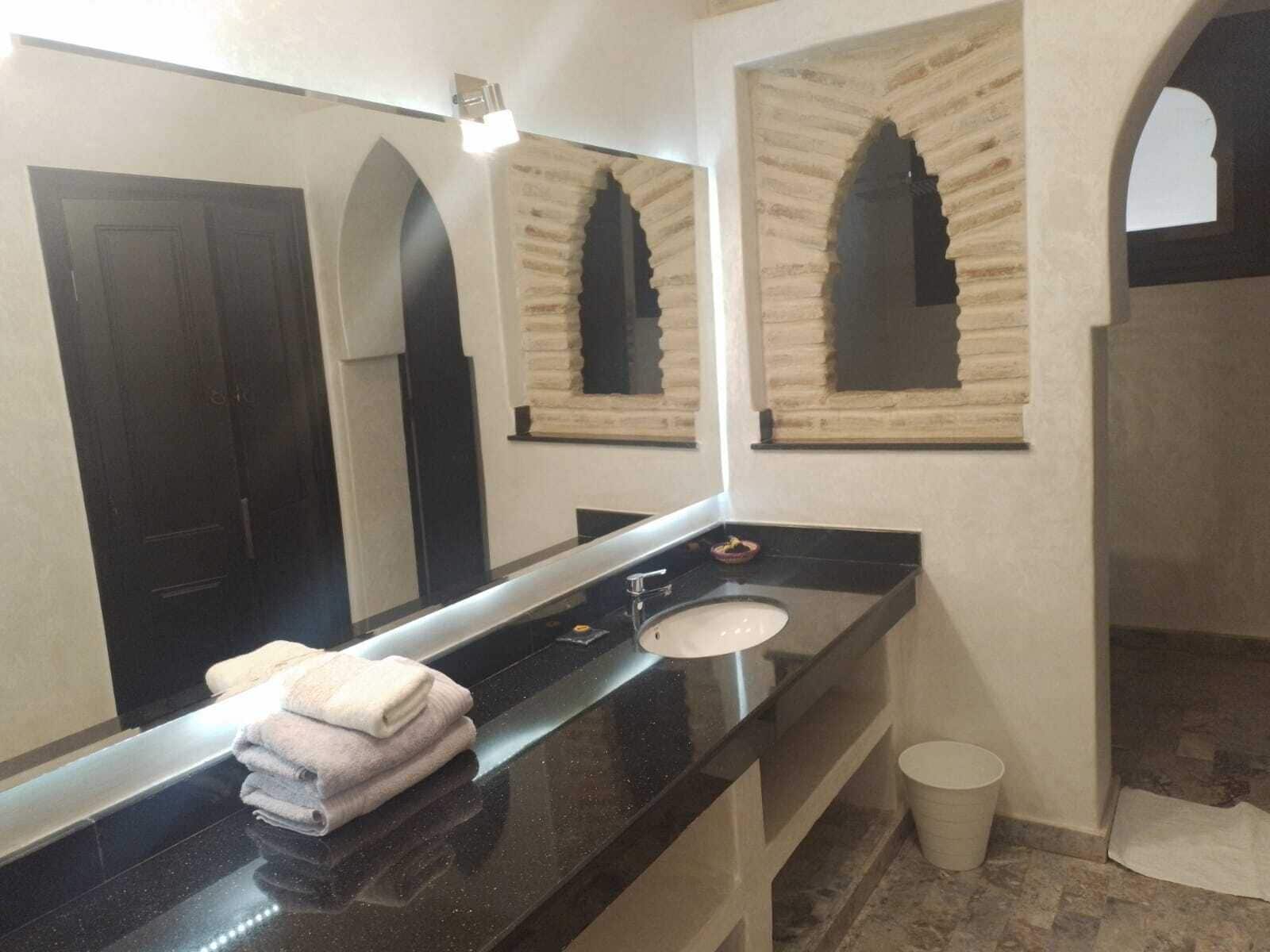 A bathroom with a black countertop, a white sink, a mirror, and a towel rack.