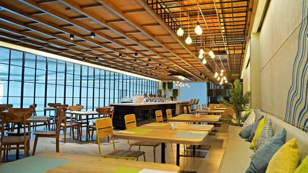 Un restaurant modern amb taules i cadires de fusta, una zona de bar i grans finestres que ofereixen una vista.