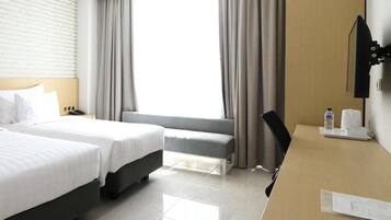 A hotel room with two beds, a desk, a chair, a TV, and a window with curtains.