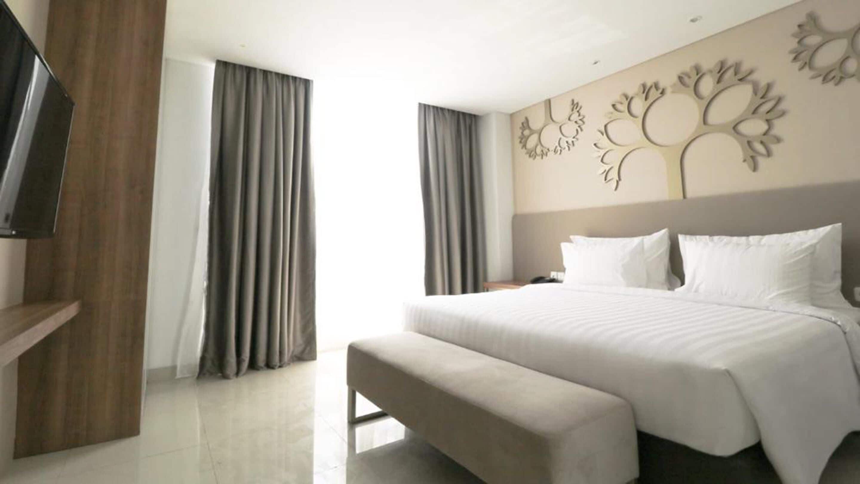A modern hotel room with a large bed, a bench, a flat-screen TV, and a decorative wall panel.