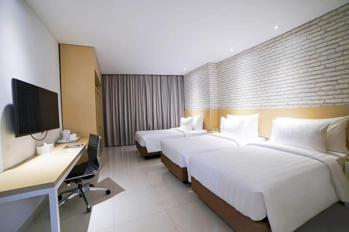 Ein Hotelzimmer mit zwei Betten, einem Schreibtisch mit Stuhl, einem Fernseher und einer Wand mit Ziegelmuster.