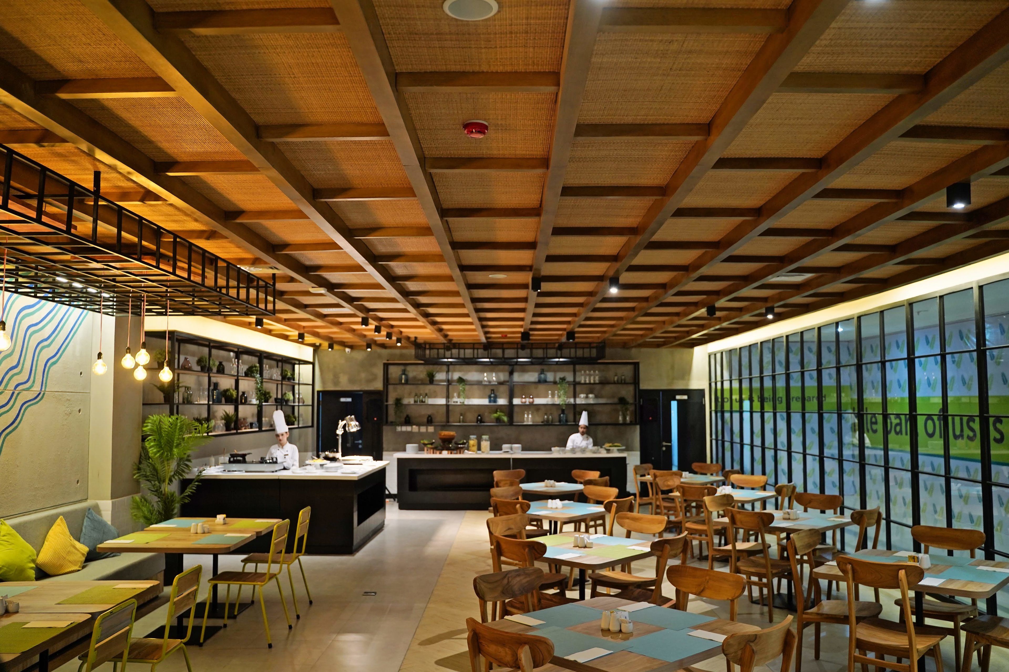 A restaurant with a modern interior, featuring wooden beams on the ceiling, a central bar area, and multiple seating arrangements.