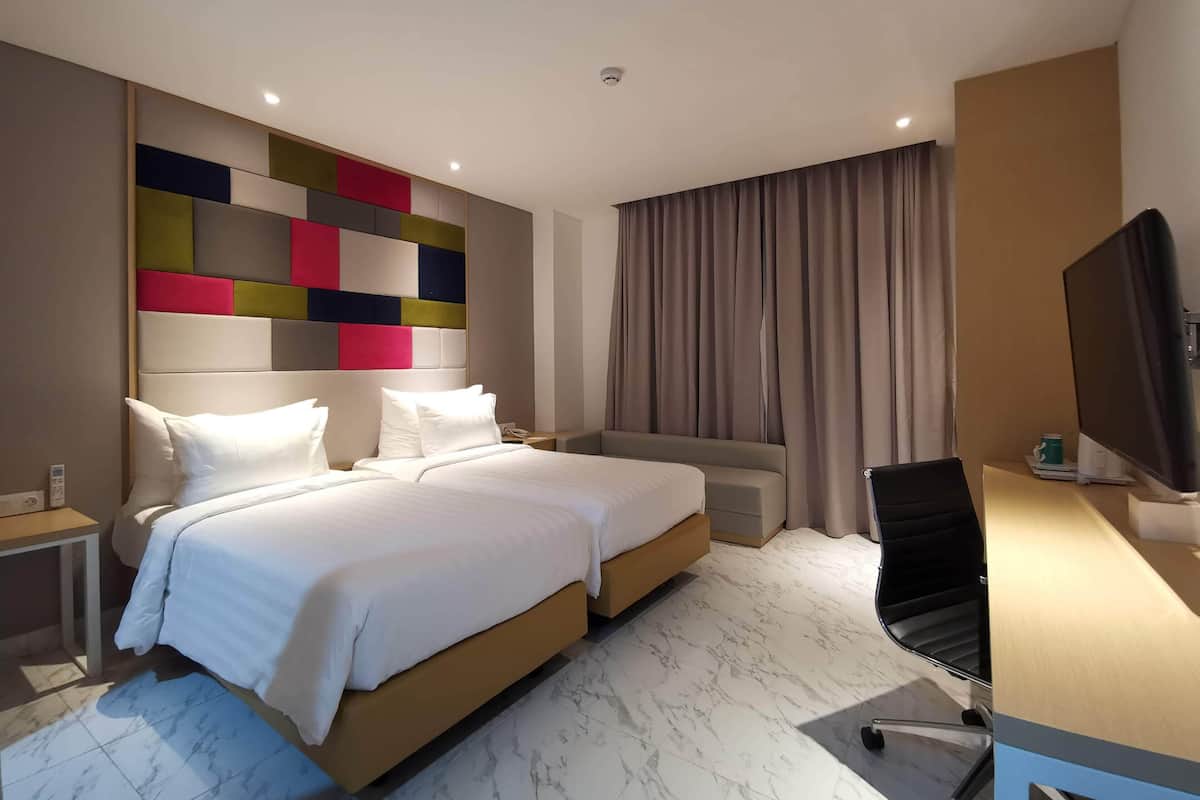 Ein Hotelzimmer mit einem großen Bett, einem Schreibtisch mit Computer, einem Fernseher und einem modernen Kopfteil.