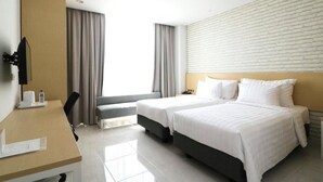 Habitació d'hotel amb dos llits, escriptori, cadira, televisió i finestra amb cortines.