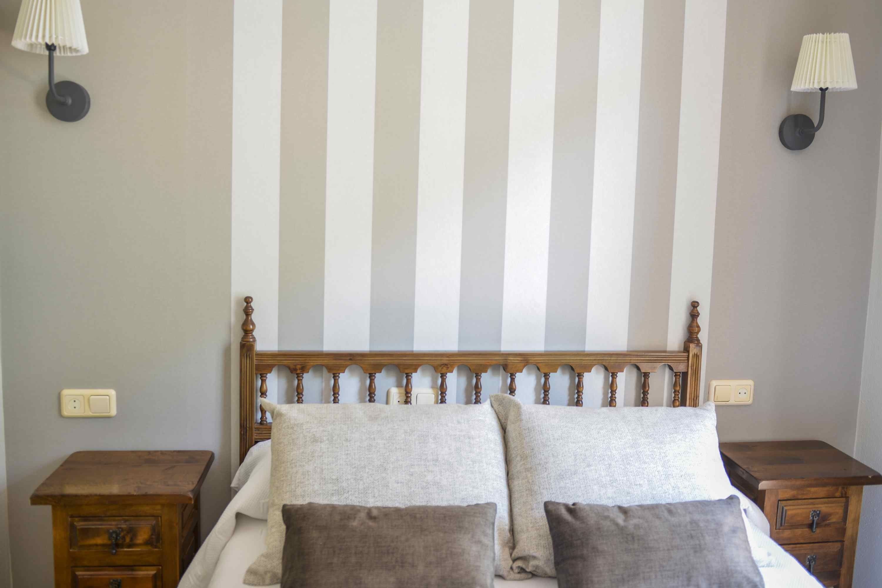 Een slaapkamer met streepjesbehang, een houten hoofdbord, twee nachtkastjes en twee lampen.