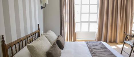 Una cama bien hecha con cabecera de madera, una mesita de noche y una silla.