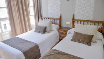 Een hotelkamer met twee bedden, elk met een houten hoofdbord, een nachtkastje en een raam met gordijnen.