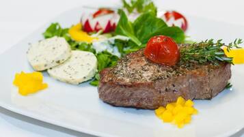 A plate with a steak, radishes, and a small tomato on a white plate.